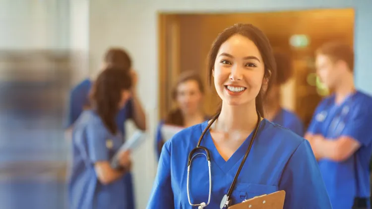 Woman in scrubs smiling and holding a clipboard